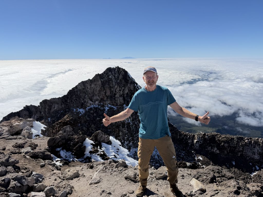 Posing on summit Taranaki with Tongariro, Ngauruhu and Ruhapehu on the horizon